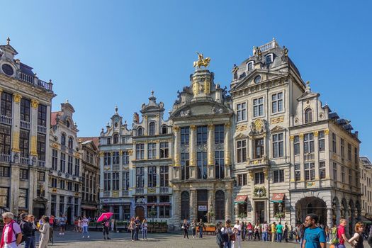 Brussels, Belgium - June 22, 2019: Grand Place with tourists and beige stone facades, gables and golden statues of southwest side against blue sky. Most famous, Arbre d’or, Etoile, Le Cygne,