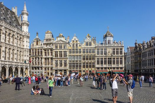 Brussels, Belgium - June 22, 2019: Grand Place with tourists and beige stone facades, gables and golden statues of northwest side against blue sky. City hall on left.