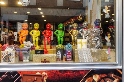 Brussels, Belgium - June 22, 2019: Large chocolate Manneken Pis statues in different colors posing on top of collection of chocolat gifts in window of confectionery store.