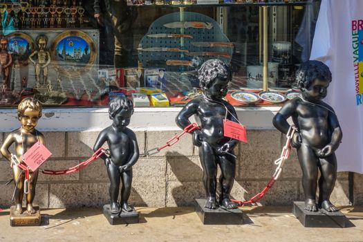 Brussels, Belgium - June 22, 2019: Closeup of chained group of metalic Manneken Pis statues in front of gift store and its display window.