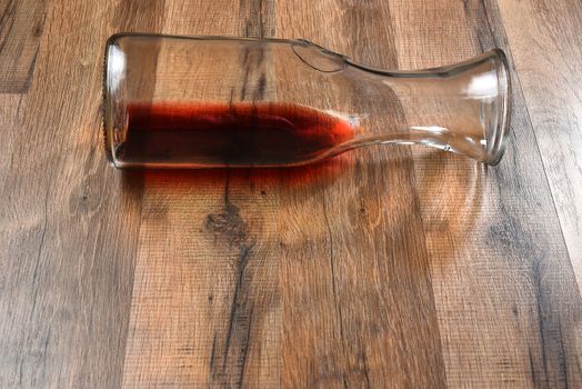 High angle view of a carafe of wine on its side on a wood table.