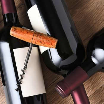 Overhead shot of three wine bottles and corkscrew on wood table. Square format.