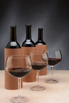 Three different wine bottles and wine glasses set up for a blind wine tasting. The bottles are covered by blank cylinders to hide the label. Vertical format. Wine glasses are partially filled with red wine.