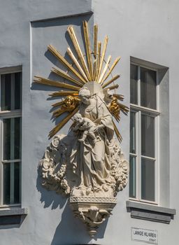 Antwerpen, Belgium - June 23, 2019: Closeup of white stone with golden rays statue of Madonna with child on corner of Meir and Lange Klarenstraat. Gray facade with windows.