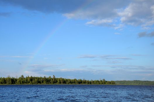 Video shows saturated and colorfull rainbow under single cloud in the sky over lake's surface