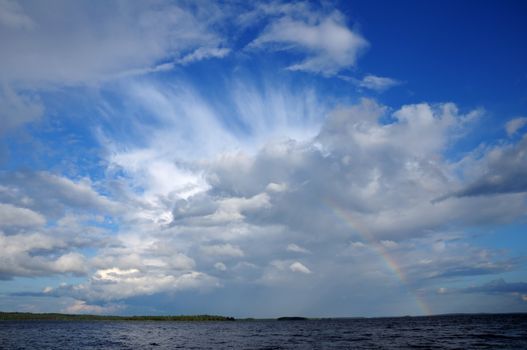 Video shows saturated and colorfull rainbow under beautiful cloud in the sky over lake's surface