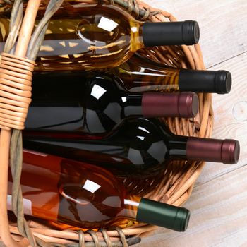 Overhead shot of several wine bottles in a basket on a whitewashed wood farmhouse style kitchen table. Square format.