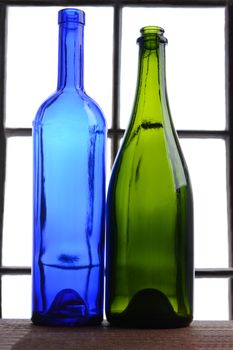 Empty wine bottle still life. A blue and a green wine bottle in front of a window.
