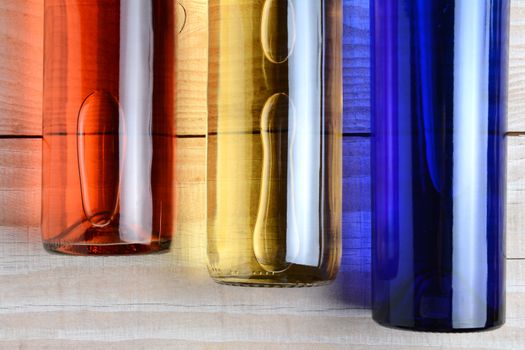 High angle shot of  red, white, and blue wine bottles on a rustic white wood table. The bottles have no labels. Horizontal format.
