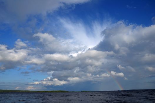 Picture shows saturated and colorful rainbow under beautiful cloud in the sky over lake's surface