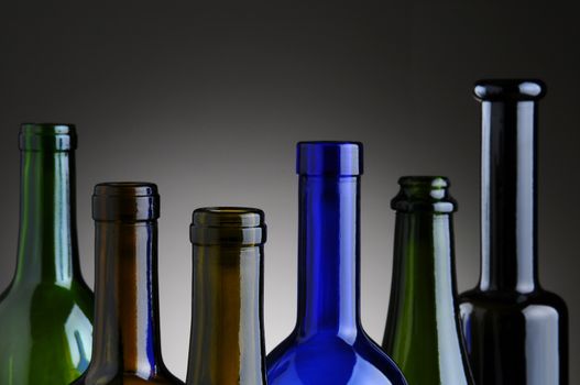 Closeup of a group of empty wine bottles over a light to dark gray background.