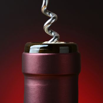 Closeup of the neck of a wine bottle with a corkscrew partially in the cork.  Over a light to dark red background in square format.