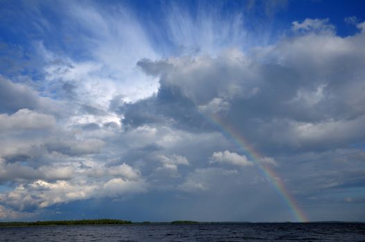 Picture shows saturated and colorfull rainbow under beautiful cloud in the sky over lake's surface