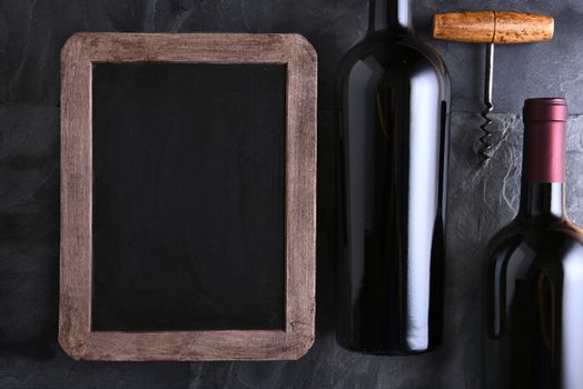 Top view of a blank chalk board for a wine list or menu with two wine bottles and old cork screw. Side light on a slate table. 