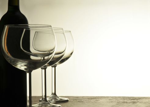 A row of Empty Wine Glasses with red wine bottle in silhouette behind horizontal format with warm light