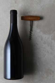Flat lay still life of a pinot noir shaped wine bottle with cork screw on a concrete table with copy space.