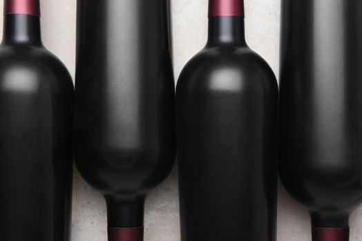 Cabernet Wine Bottles: Closeup overhead shot of four red wine bottles in alternating orientation on concrete table top.