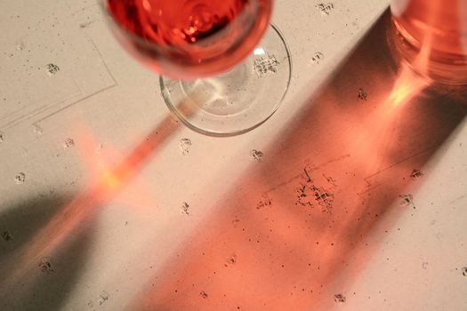 High angle view of a red wine bottle and glass with shadows and reflections on a concrete table top.