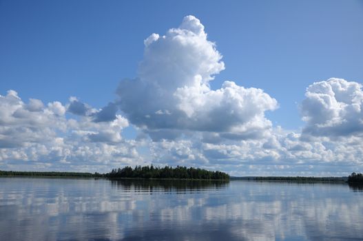 The picture shows typical landscape in the south region of Karelia - blue sky, clouds, big lake looks like a mirror and a lot of distant green islands, trees, stones and rocks