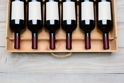 Overhead shot of a case of red wine bottles with blank labels  on a rustic white wood table with copy space at the bottom. Horizontal format.