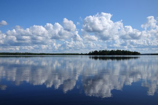 The picture shows typical landscape in the south region of Karelia - blue sky, clouds, big lake looks like a mirror and a lot of distant green islands, trees, stones and rocks