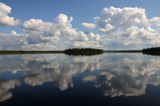 The picture shows typical landscape in the south region of Karelia - blue sky, clouds, big lake looks like a mirror and a lot of distant green islands, trees, stones and rocks