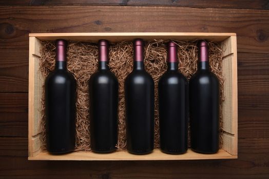 Case of Red Wine: Top view of a wood case of red wine bottles on a dark wood table, the case is filled with packing straw.