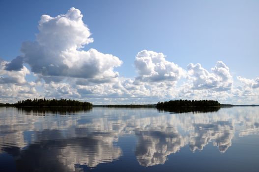 The picture shows typical landscape in the south region of Karelia - blue sky, clouds, big lake looks like a mirror and a lot of distant green islands, trees, stones and rocks