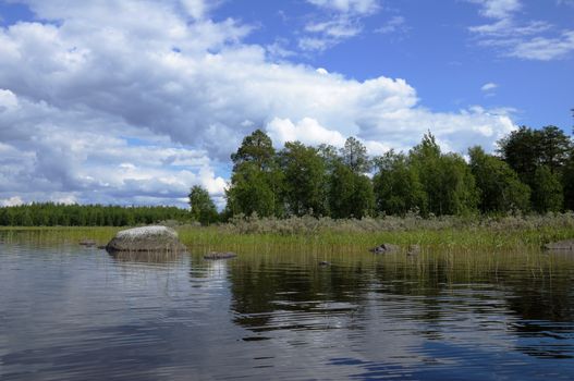 The beautiful picture of Karelian forest at the edge of a lake, and some huge boulder in this lake