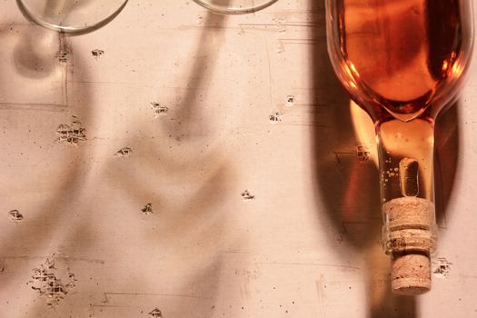 High angle view of a rose wine bottle with shadows and reflections on a concrete table top.