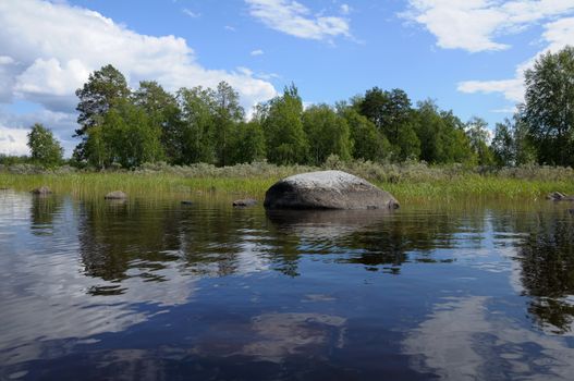 The beautiful picture of Karelian forest at the edge of a lake, and some huge boulder in this lake