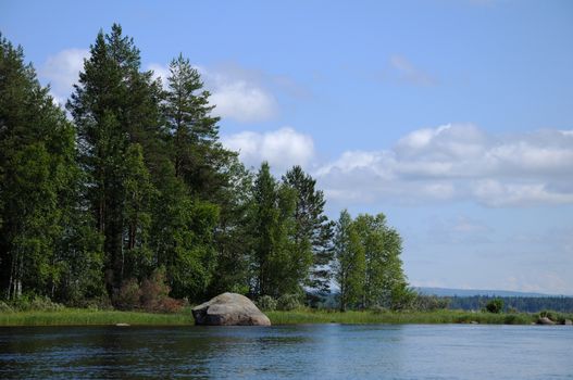 The beautiful picture of Karelian forest at the edge of a lake, and some huge boulder in this lake