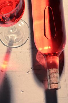 High angle view of a red wine bottle and glass with shadows and reflections on a concrete table top.