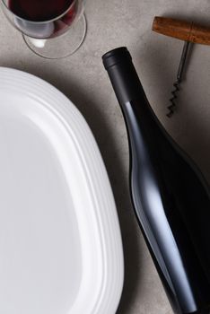 Flat lay arrangement of a dinner table with a bottle of red wine and white platter. The bottle has no label.
