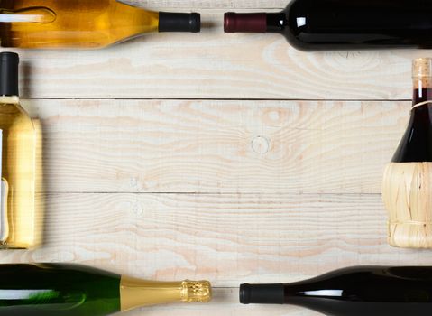 High angle shot of a group of wine bottles on a rustic white wood table. The bottles are laying on their sides and end to end to form a rectangle frame with a blank center.
