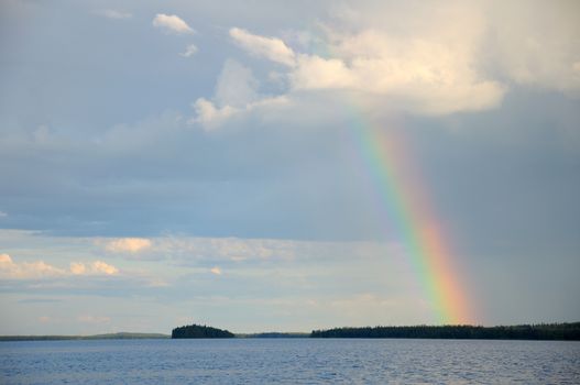 Picture shows saturated and colorful rainbow under single cloud in the sky over lake's surface