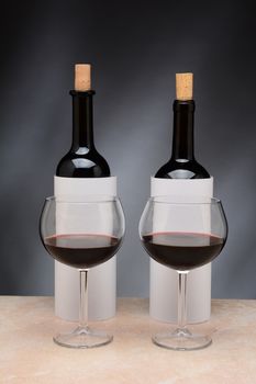 Two different wine bottles and wine glasses set up for a blind wine tasting. The bottles are covered by blank cylinders to hide the label. Vertical format. Wine glasses are partially filled with red wine.