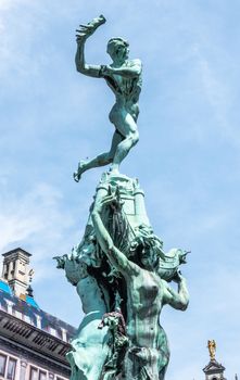 Antwerpen, Belgium - June 23, 2019: Top of Green bronze Brabo statue on Grote Markt, with historic houses  gables in back under blue sky.