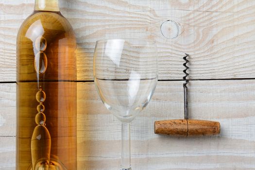 High angle closeup of a bottle of white wine next to a wineglass and corkscrew on a whitewashed rustic table. Horizontal format.