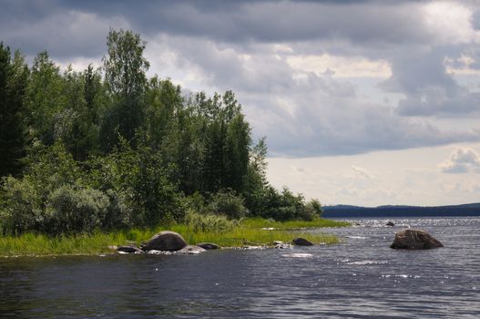 The beautiful picture of Karelian forest at the edge of a lake, and some huge boulder in this lake