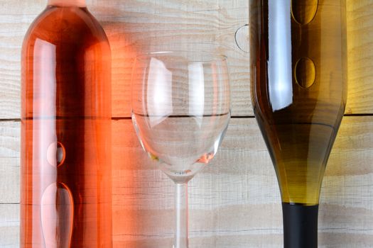 Closeup of a wine glass between a bottle of red wine and a bottle of white wine. All three objects are laying on a rustic white wood table. Horizontal format from a high angle.