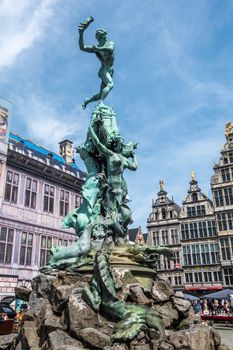 Antwerpen, Belgium - June 23, 2019: Green bronze Brabo statue on Grote Markt, with historic houses and gables in back under blue sky.
