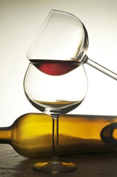 Two stacked wine glasses in front of a empty horizontal bottle with warm tones and lighting.