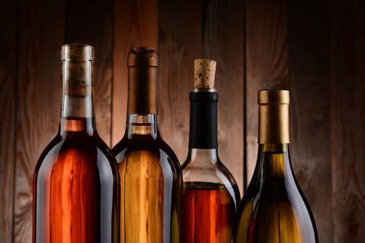 Four wine bottles against a wood background. The bottles have no label and the texture of the background shows through. Horizontal format. showing only the top of the bottles.