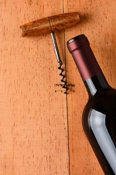 Cabernet bottle and corkscrew on a rustic wooden surface. The antique opener and bottle are at an angle leaving plenty of copy space. Only half the bottle is in the frame.