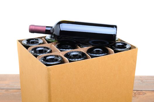 Closeup of a case of wine with one bottle resting on top. Case is sitting on a wood table top with a white background.