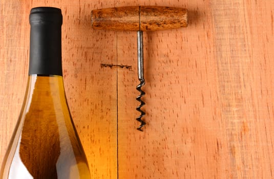 Closeup of a Chardonnay wine bottle and corkscrew on a rustic wood surface. The bottle has no label and there is plenty of room for copy.
