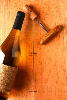 A chardonnay wine bottle and corkscrew on a rustic wood surface. Viewed from above the bottle is partially out of frame leaving plenty of copy space. The image has strong warm side light. 