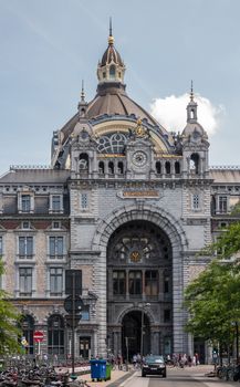 Antwerpen, Belgium - June 23, 2019: monumental gray stone building and De Keyserlei entrance of Central Railway Station. Streetview with car and people under light blue sky.