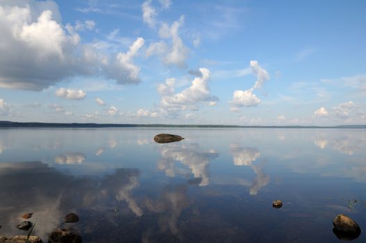 The picture shows typical landscape in the south region of Karelia - blue sky, clouds, big lake looks like a mirror and a lot of distant green islands, trees, stones and rocks